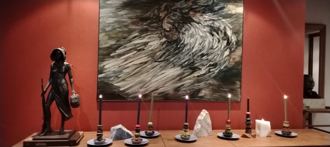 Row of lit stacked candles along a sideboard beneath a large painting