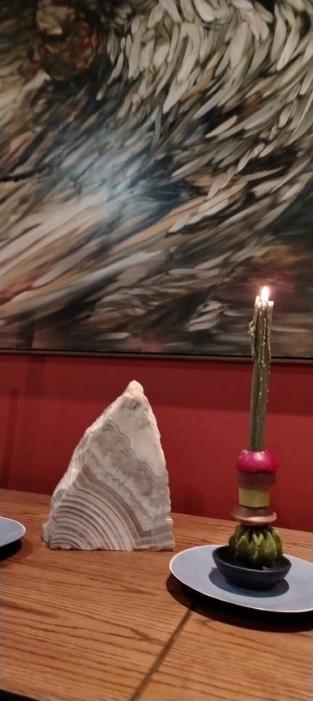 Single lit stacked candle on a saucer against a red wall and artwork