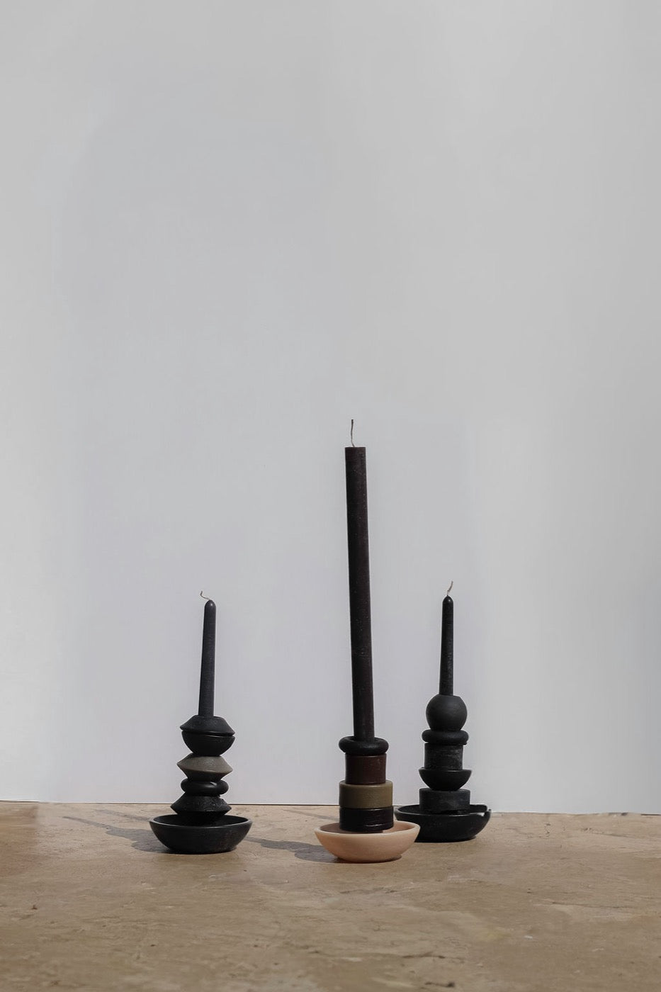 Three black stacked candles against a white wall