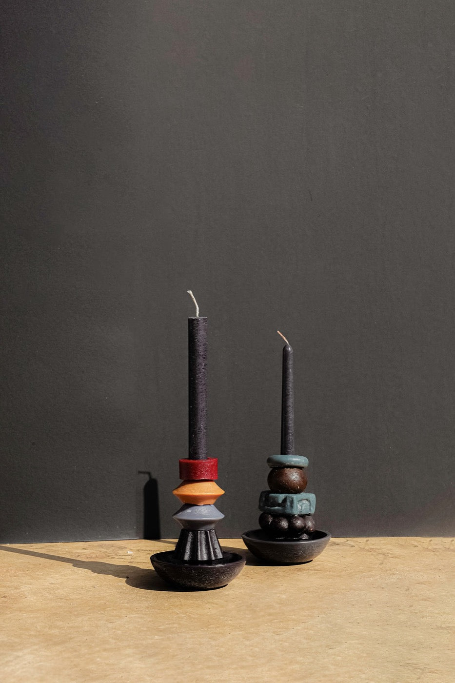 Two black tapers in red, orange and teal stacked holders