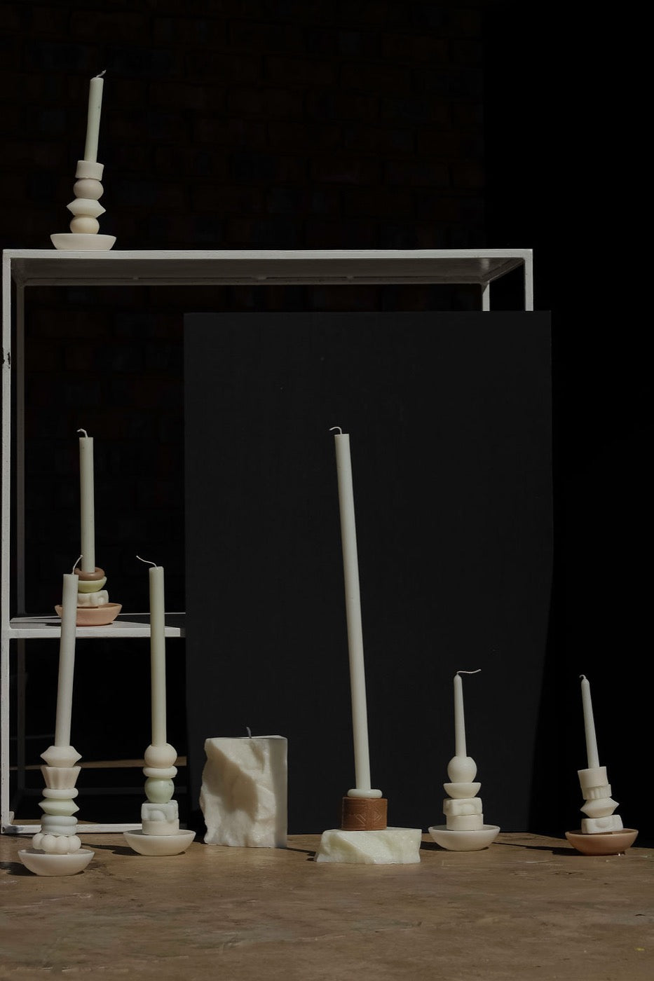 Ivory candle collection arranged on a white shelf against exposed brick