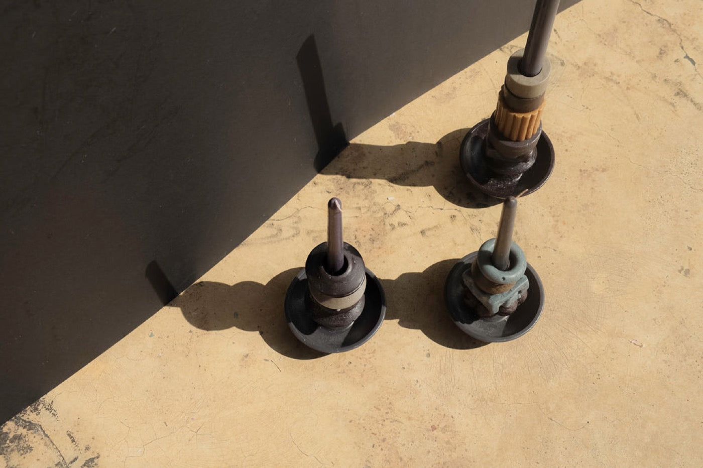 Three dark stacked candles from above on a sunlit concrete floor
