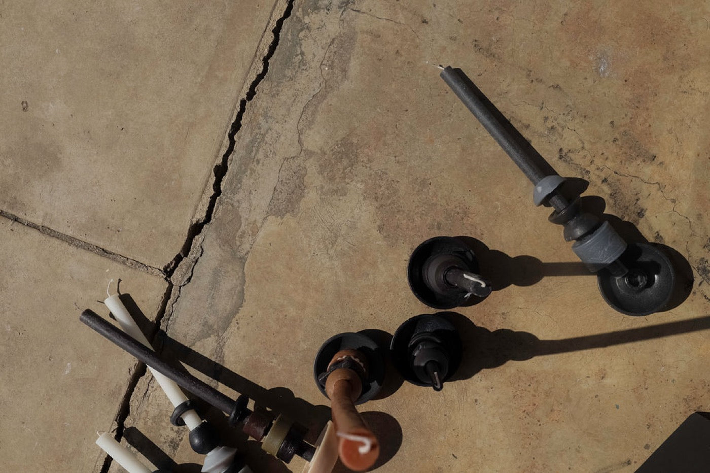 Candle holders and loose tapers scattered across cracked concrete