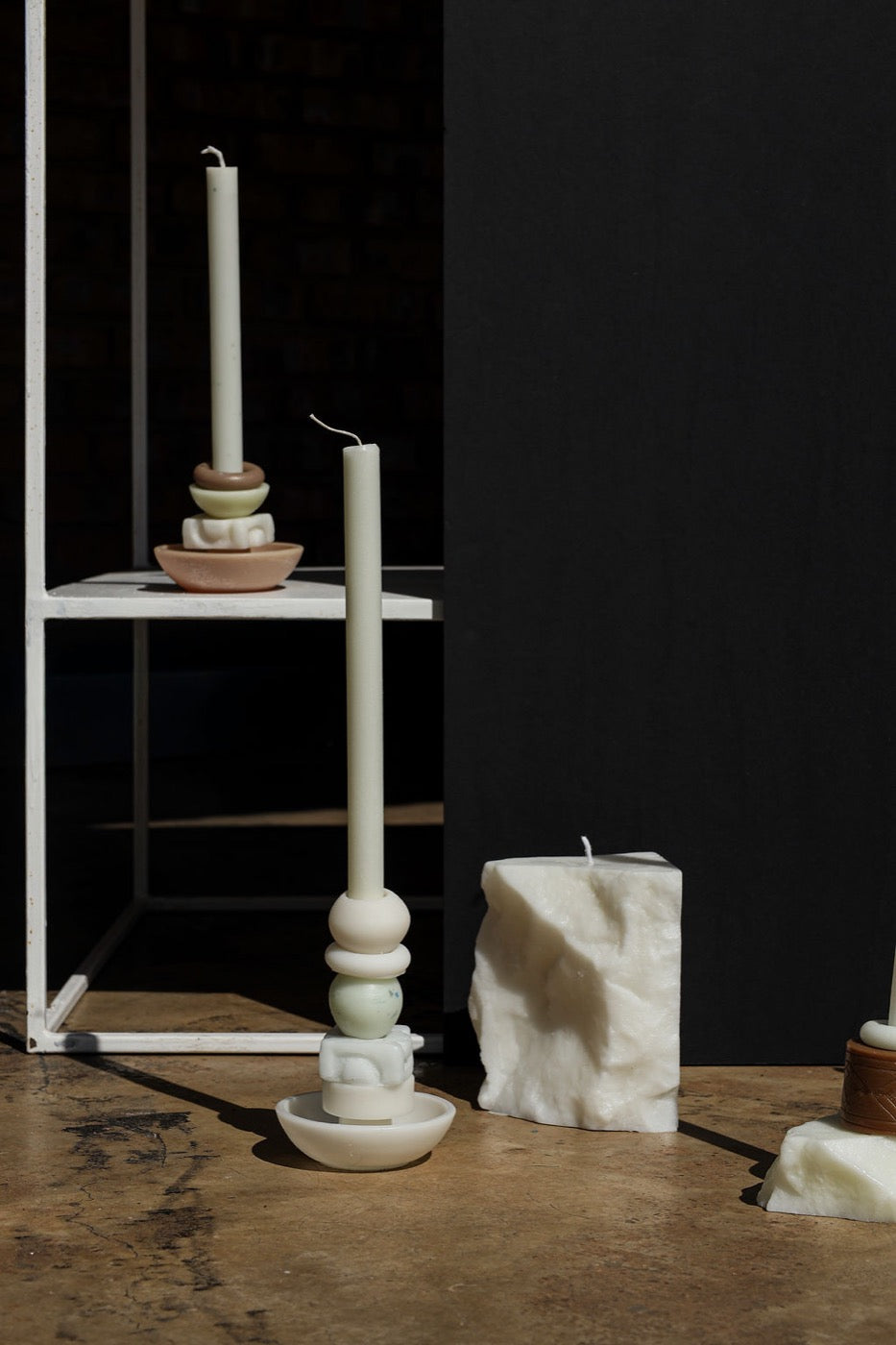 Ivory stacked candles beside a wax block, one raised on a white shelf