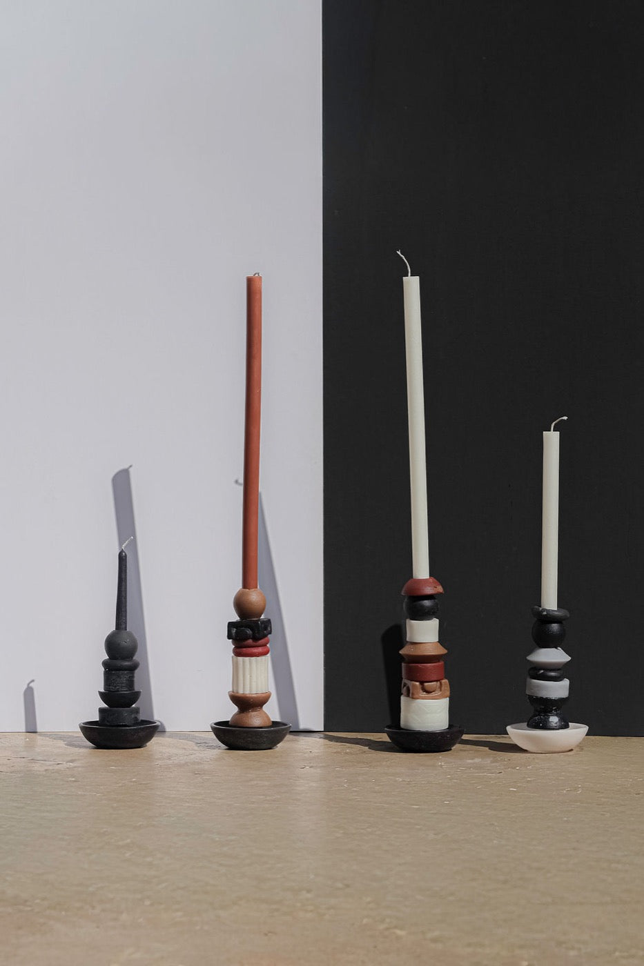 Four stacked candles in black, terracotta and grey against black and white panels