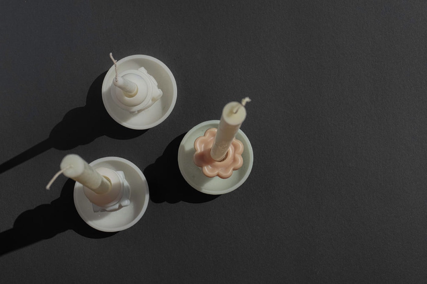 Overhead view of three pale candle holders on a dark surface