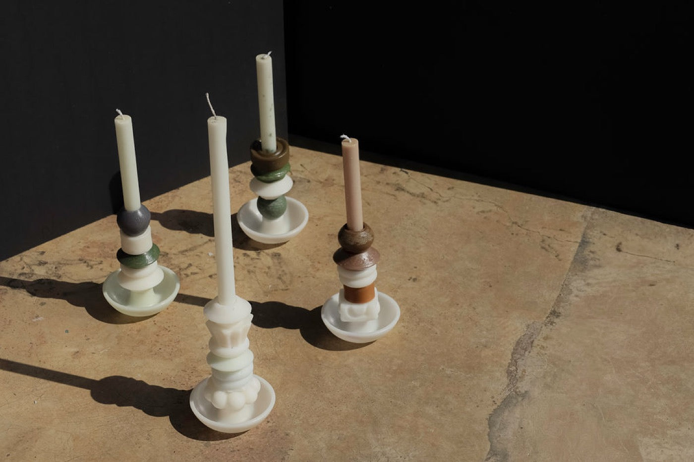 Four pale stacked candles on sunlit concrete beside a white plinth