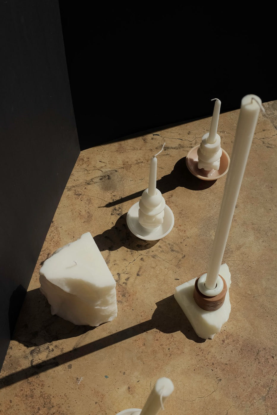 Overhead view of pale candle holders and a wax block on warm concrete