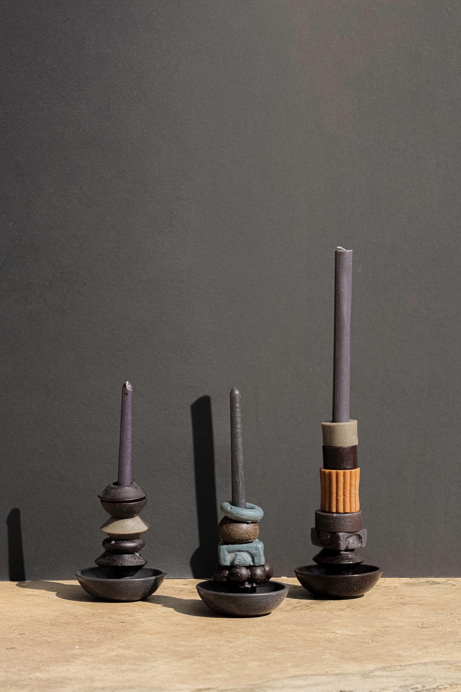 Three stacked candles in plum, bronze and teal on dark bowl bases