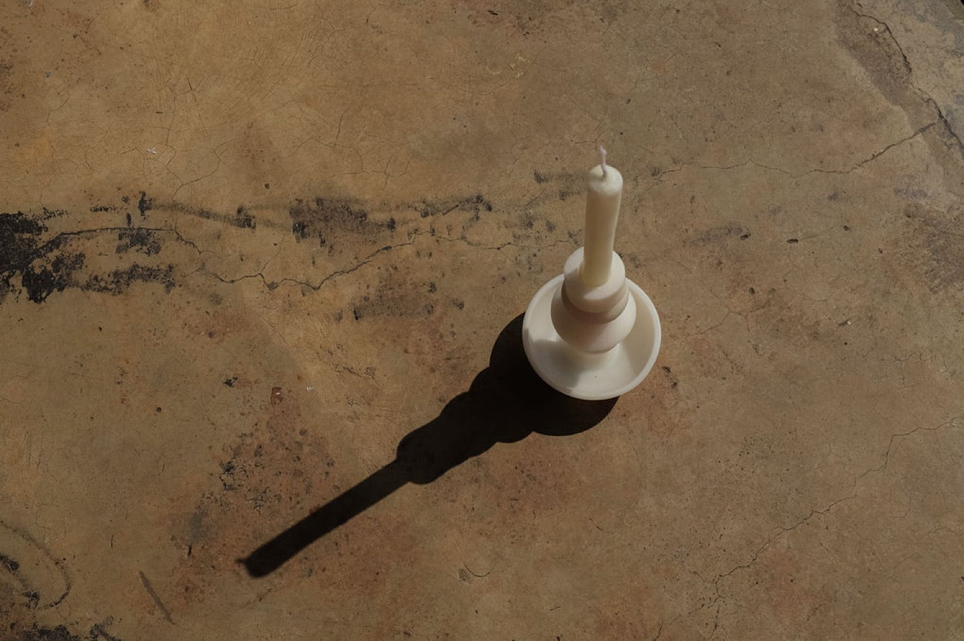 Single white stacked candle from above on a concrete floor