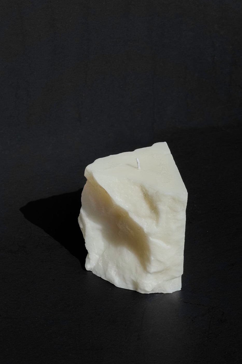 Rough-hewn ivory wax block candle on a black surface
