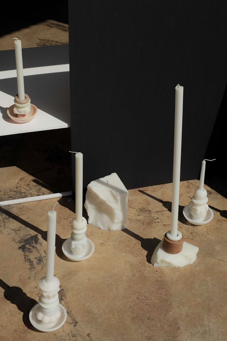 Collection of white stacked candles and a wax block in raking sunlight