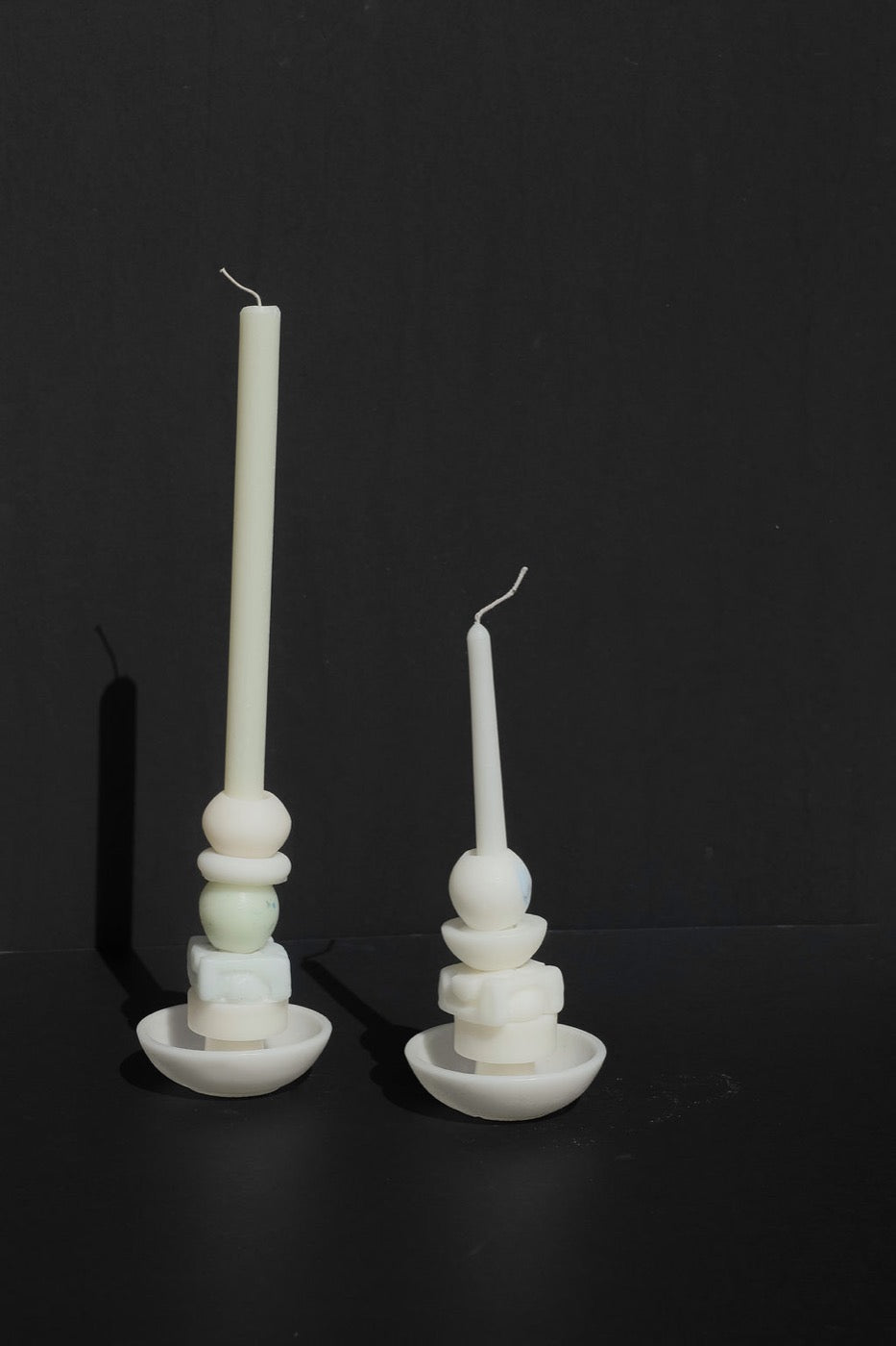 Two white stacked candles of different heights on black