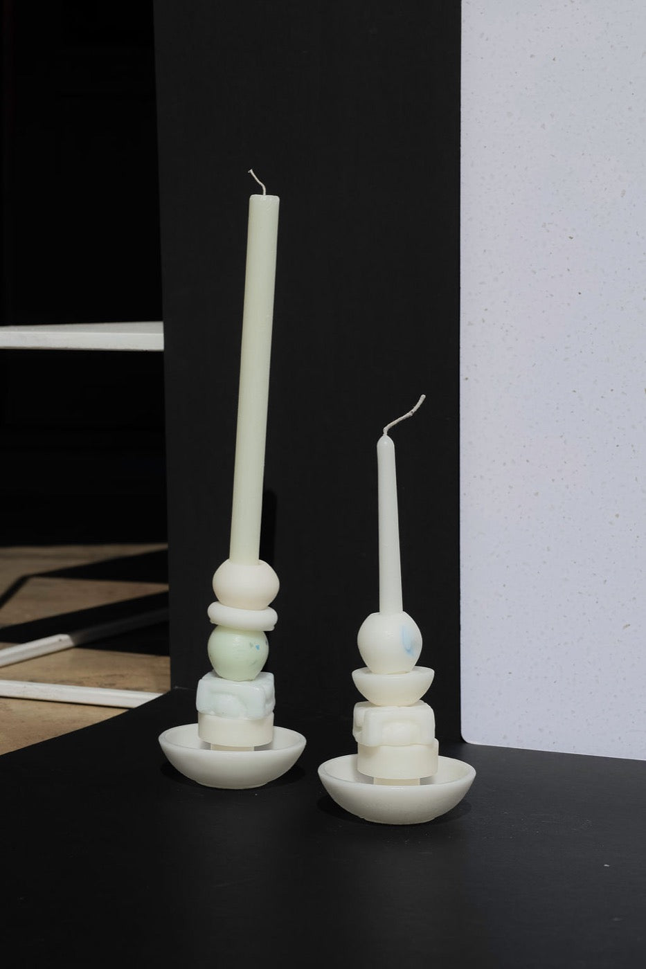 Two white stacked candles in a studio corner beside a terrazzo panel
